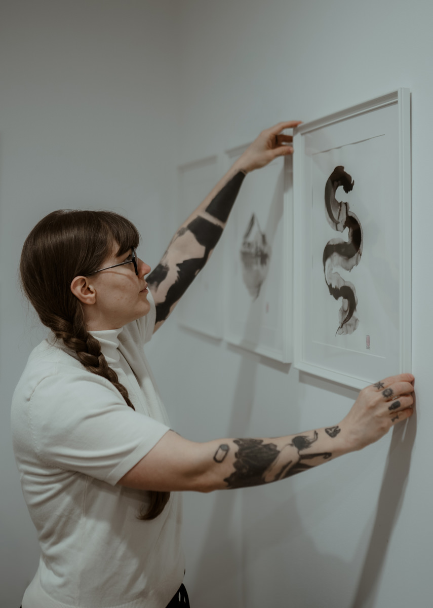 Agnes Hayden hanging one of her abstract ink paintings in a gallery.