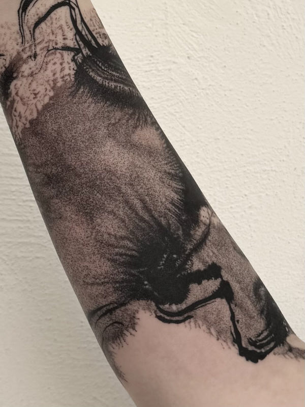 Close up view of abstract lower arm wrap around tattoo by Agnes Hayden, showing black brush strokes and light grey textures.